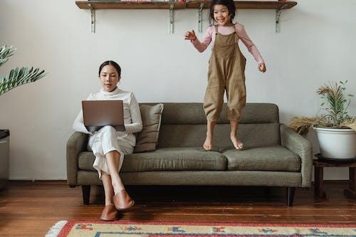 Parent using laptop and child standing on sofa